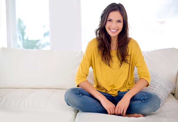 A woman with a bright white smile sitting on sofa at Surf City Oral and Maxillofacial Surgery in Huntington Beach, CA