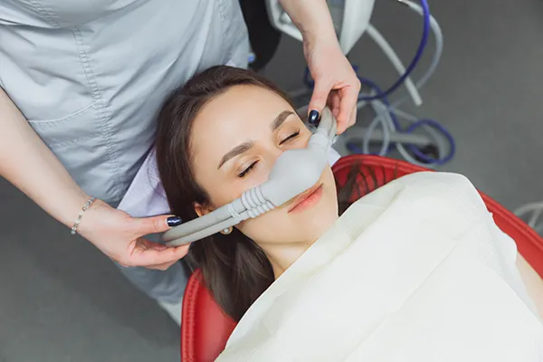 Dental assistant fitting a sedation mask over the nose of her calm female patient at Surf City Oral and Maxillofacial Surgery in Huntington Beach, CA