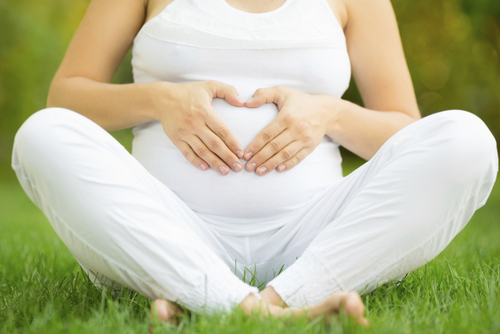 A pregnant woman sitting on grass and holding her stomach at Surf City Oral and Maxillofacial Surgery in Huntington Beach, CA