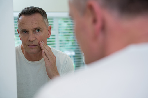 A man looking at his face in the mirror wondering if he has oral cancer